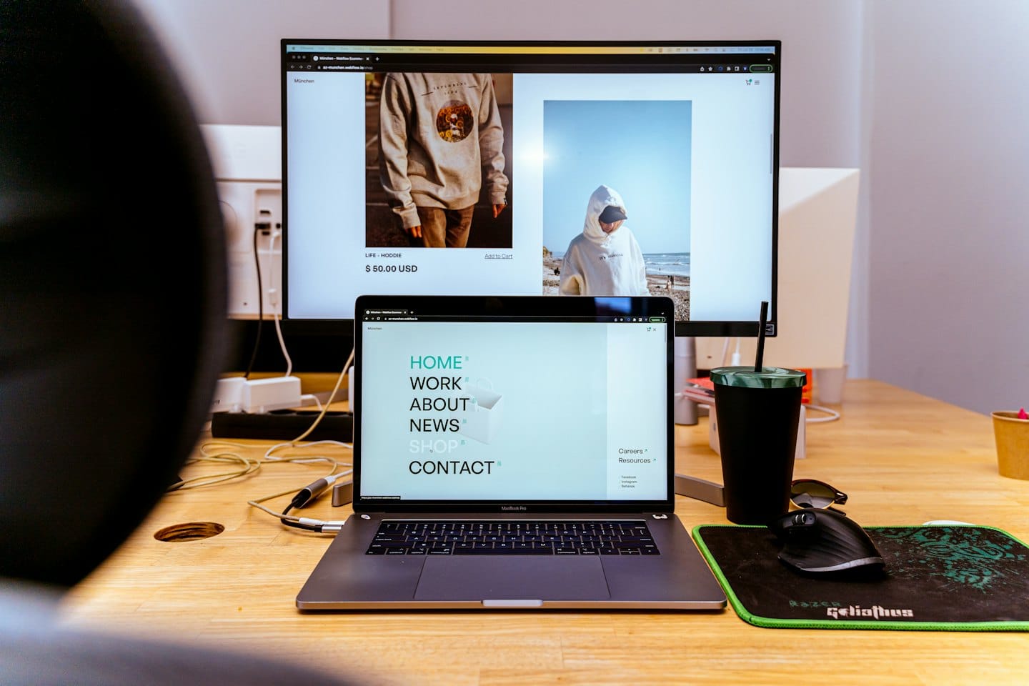 Osoba pracująca przy laptopie i monitorze wyświetlającym stronę sklepu internetowego.