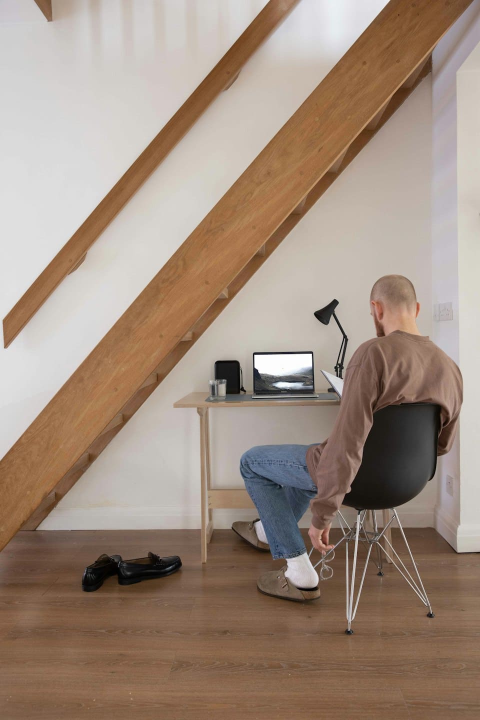 Mężczyzna pracujący na laptopie przy biurku pod schodami.